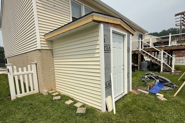 Vinyl siding going up on a new addition, with housewrap still exposed on the front wall and the exterior door hung