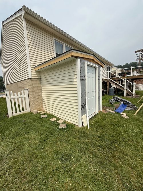 Vinyl siding going up on a new addition, with housewrap still exposed on the front wall and the exterior door hung